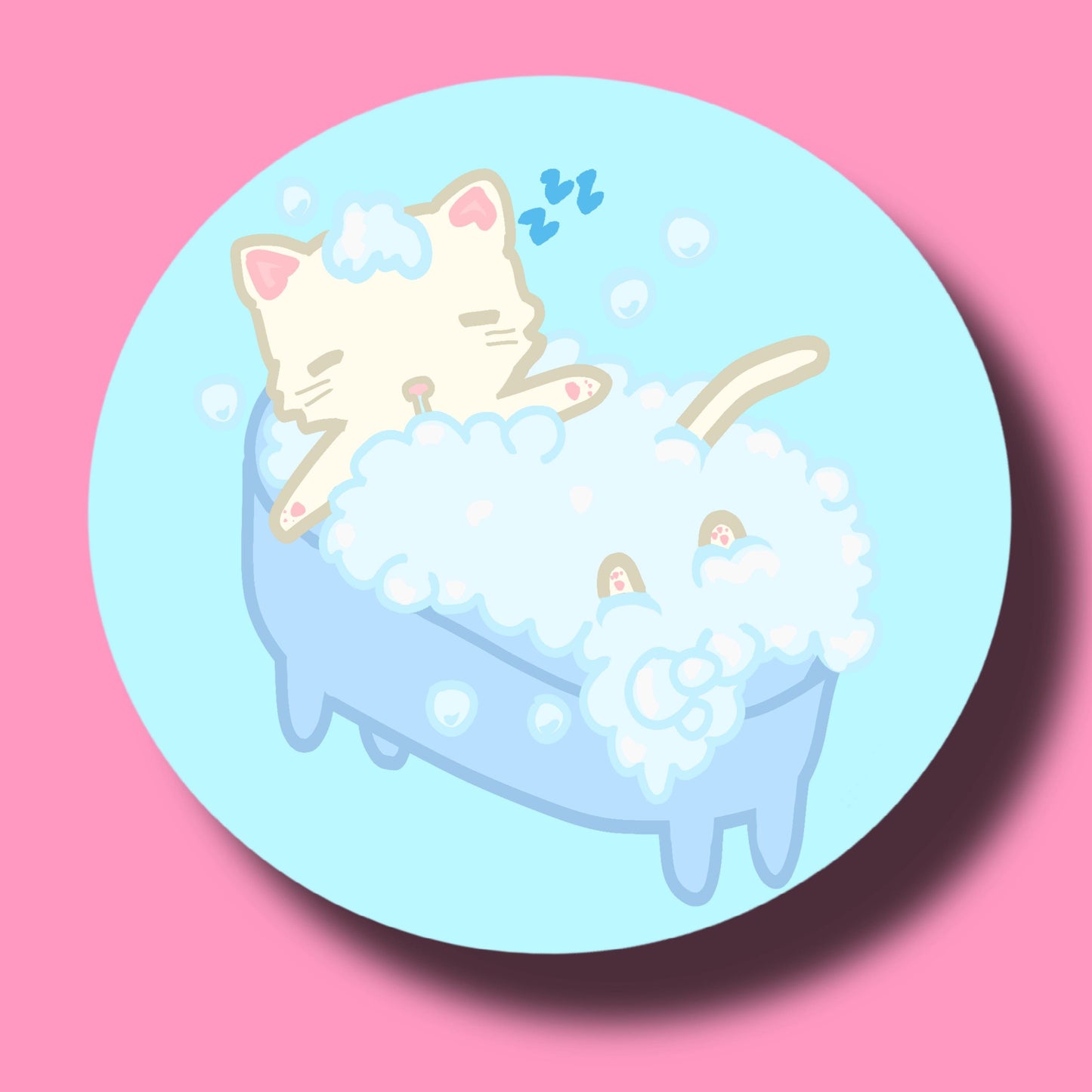 A circular sticker or coaster featuring a cute cartoon illustration of a cream-colored cat sleeping in a light blue bathtub filled with white bubbles, set against a solid pink background.