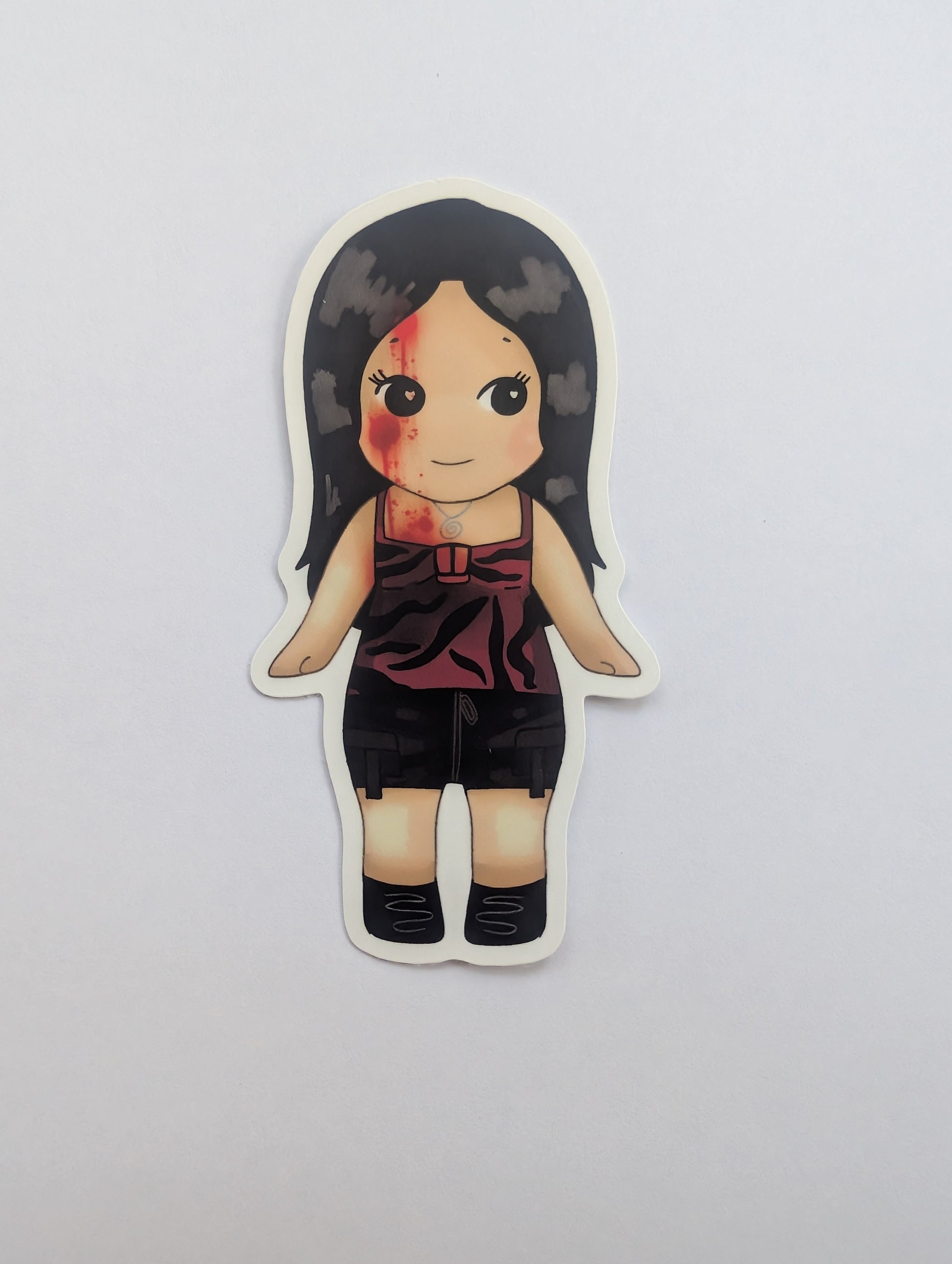 Nikki freeman keychain sonny angel. A die-cut vinyl sticker featuring a chibi-style cartoon girl with long black hair, a bloody face, and a dark red sleeveless top with black shorts, shown on a plain light gray background.