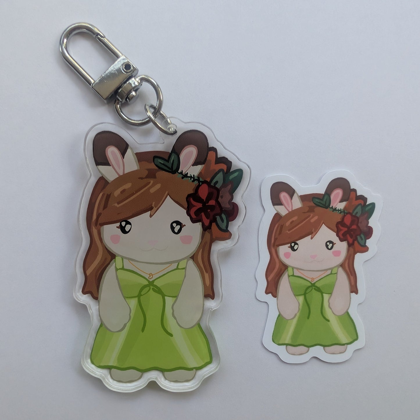 A cartoon-style jackie taylor keychain charm and matching die-cut sticker featuring a girl with brown hair, bunny ears, and a green dress, shown on a plain light background.