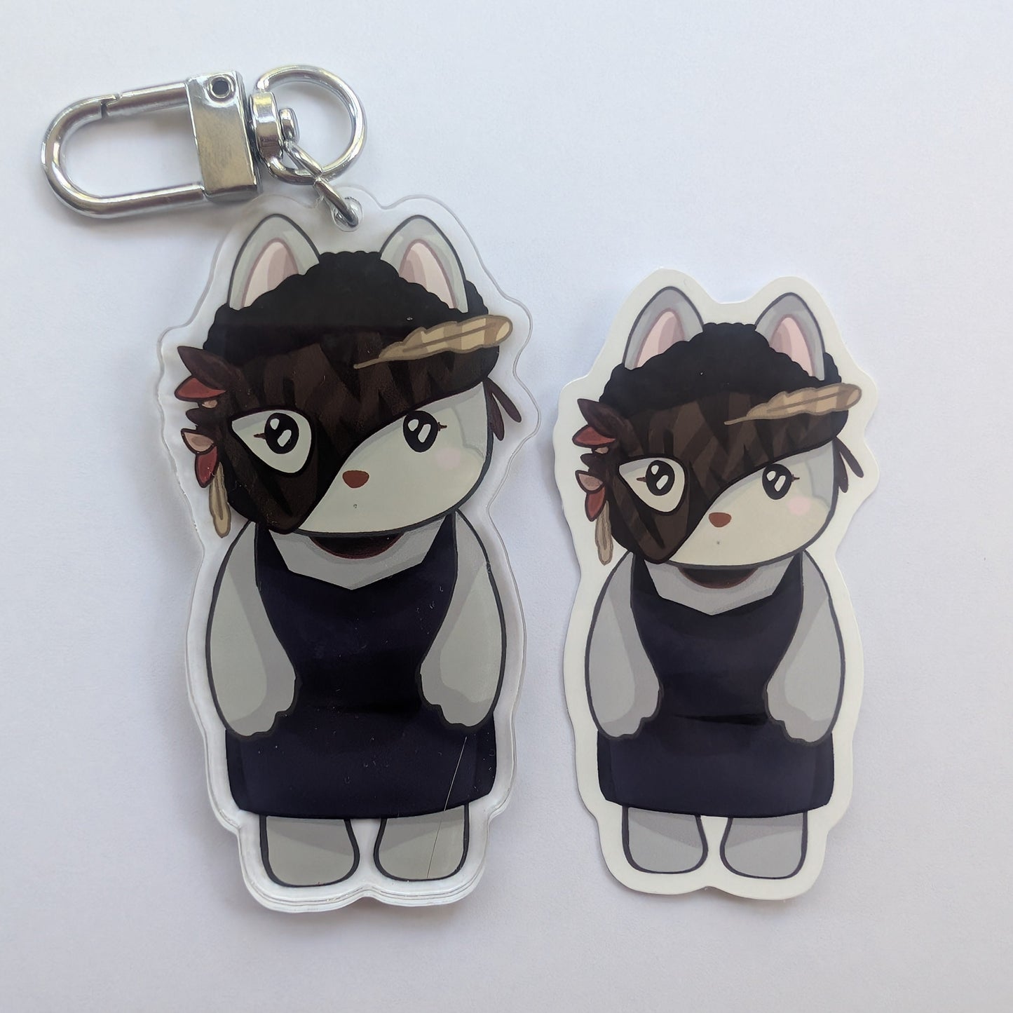 Two die-cut acrylic keychains featuring a chibi-style cat character with a dark head covering and navy dress, shown on a plain light background. One keychain includes a silver metal clasp.