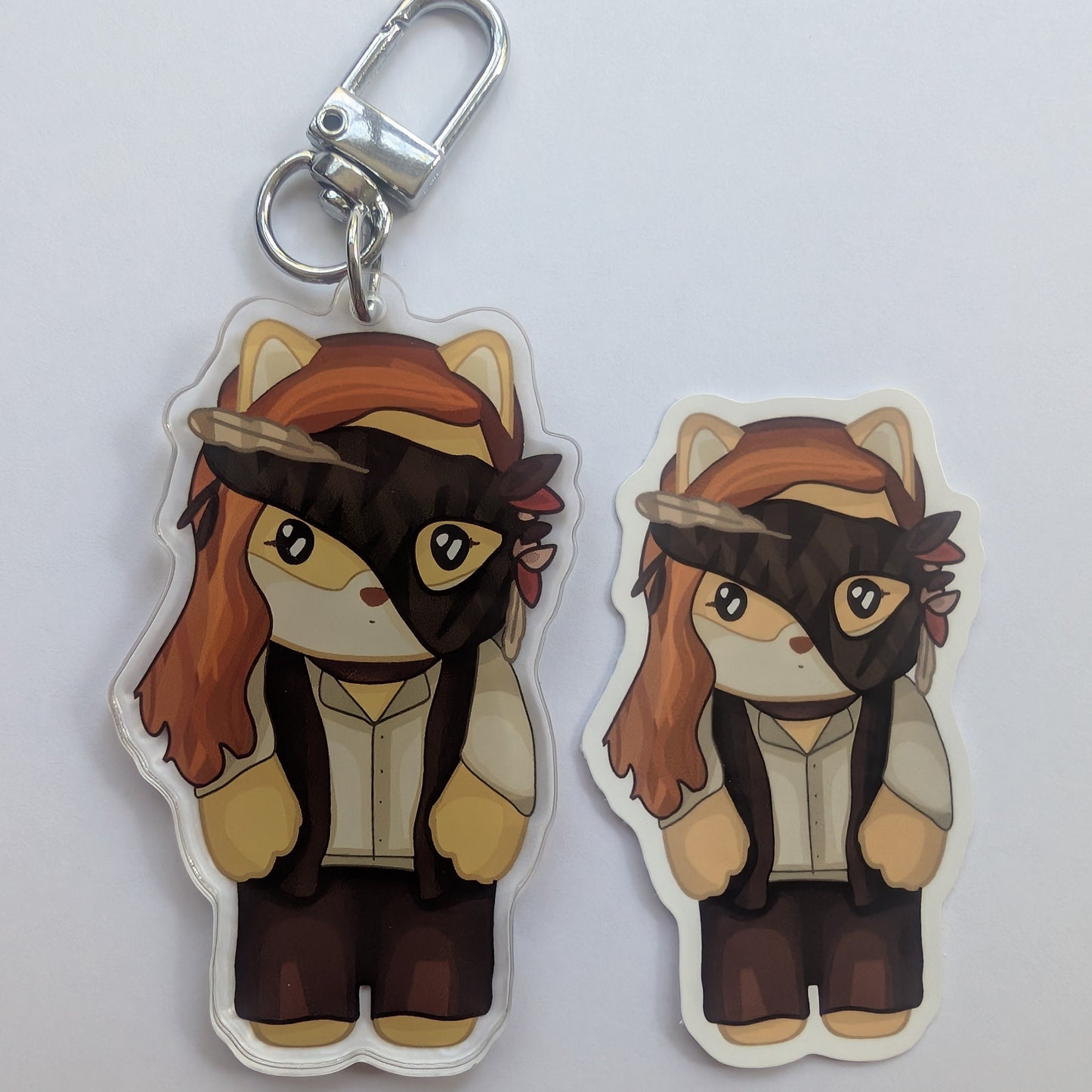One acrylic keychains van palmer featuring a chibi-style cat character with orange hair, a black eye mask, and a feather headband, shown on a plain light background.
